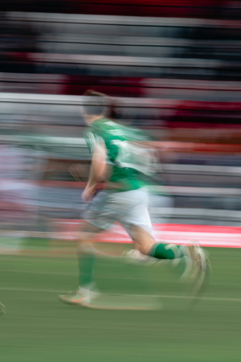 Atleta in maglia verde corre su un campo sportivo.