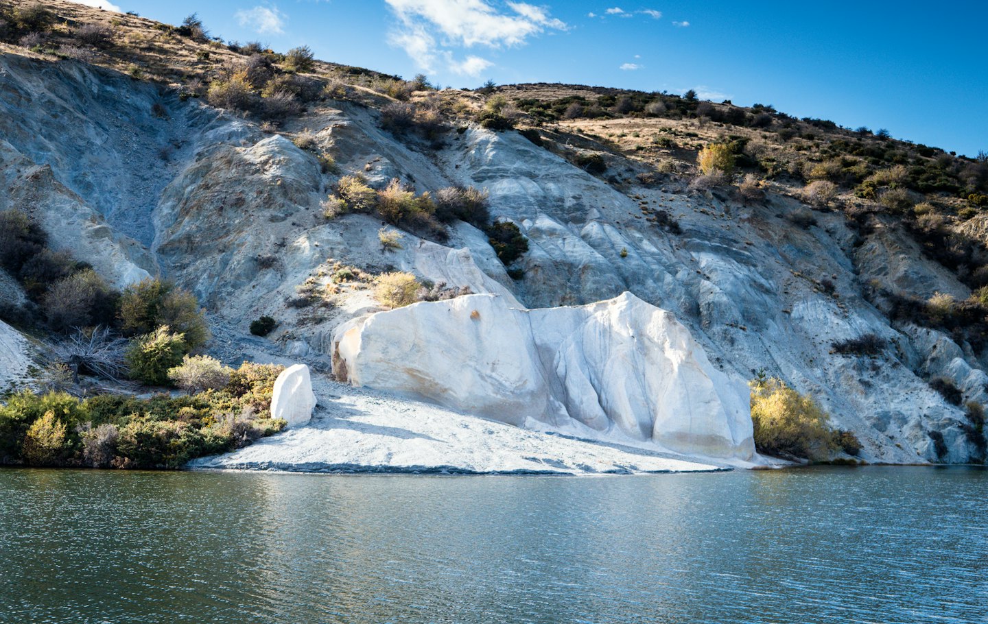 Colline aspre si ergono sopra un lago calmo con formazioni rocciose stratificate.